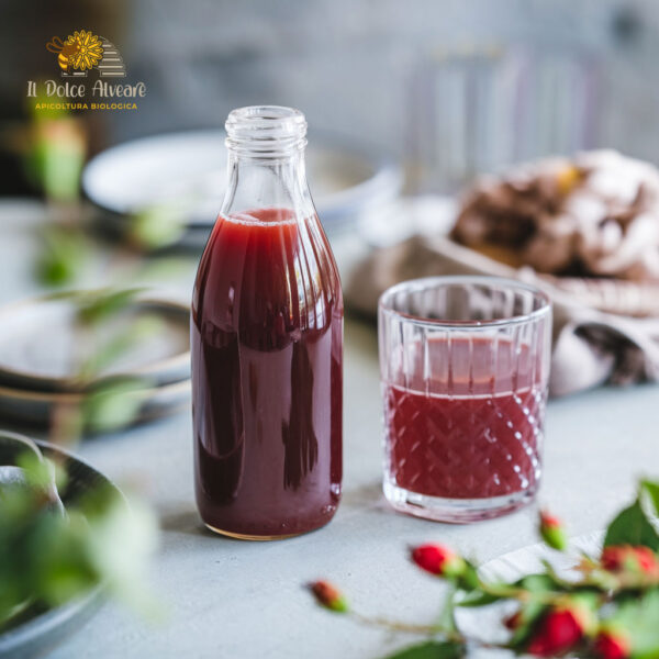 Bottiglia di succo di rosa canina su tavola apparecchiata, con bicchiere di succo accanto.